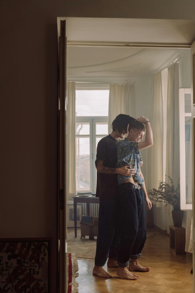 A same-sex couple sharing an intimate embrace in a cozy indoor setting, filled with natural light.